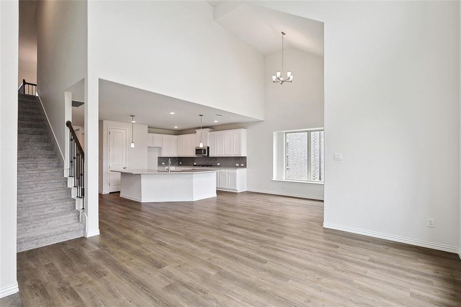 Unfurnished living room featuring light wood-type flooring, high vaulted ceiling, sink, and a notable chandelier