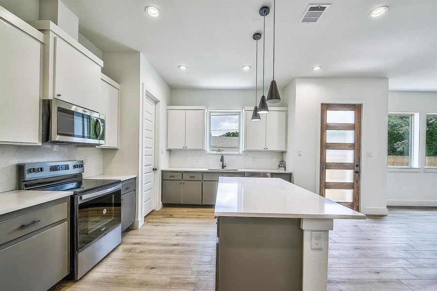 Kitchen with a kitchen island, hanging light fixtures, stainless steel appliances, sink, and light wood-type flooring