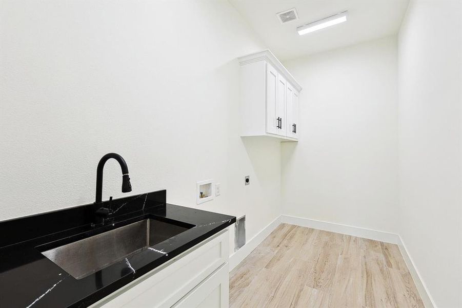 Laundry room featuring hookup for a washing machine, light wood-type flooring, electric dryer hookup, cabinets, and sink