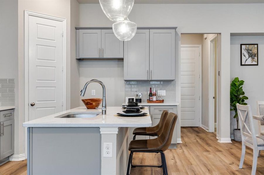 Kitchen featuring decorative backsplash, an island with sink, light wood-type flooring, decorative light fixtures, and sink