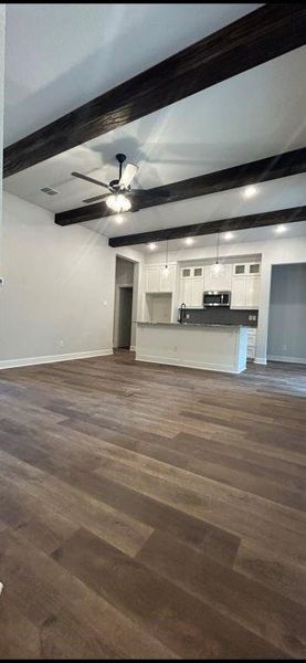 Unfurnished living room with ceiling fan, beamed ceiling, and dark hardwood / wood-style flooring