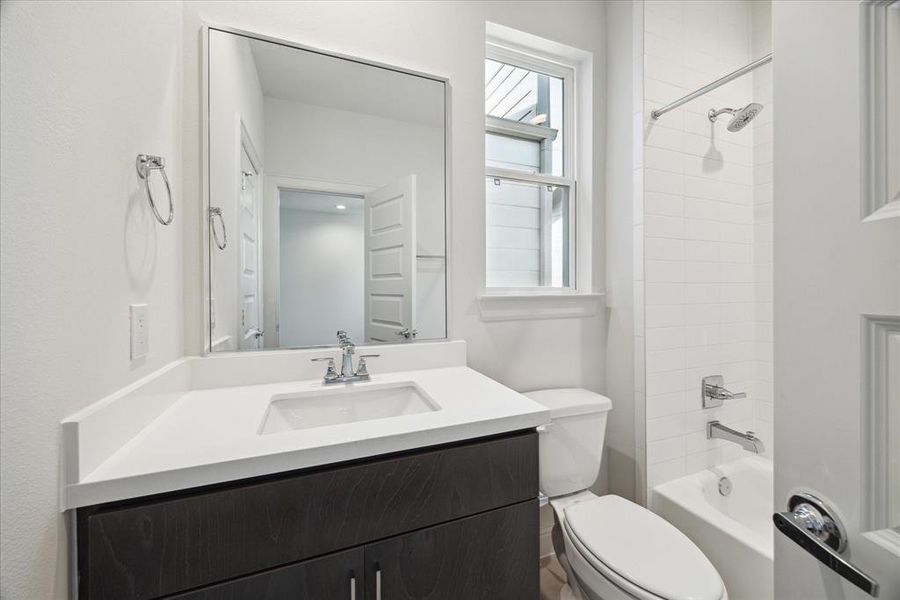 This full bathroom features a versatile shower/tub combo, perfect for relaxing baths or quick showers. The clean white subway tile adds a classic touch, while the large window brings in natural light, brightening the space. A sleek vanity with a large mirror complete the modern look.