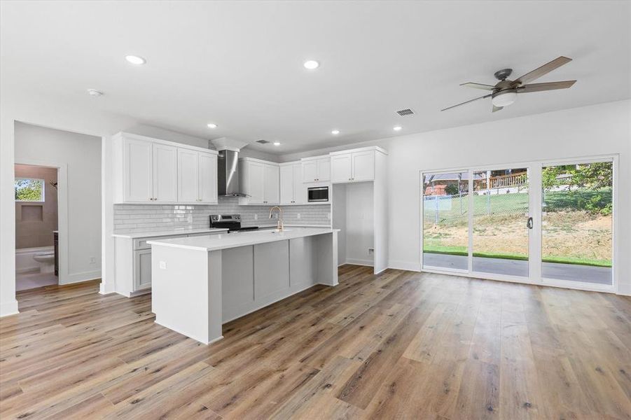 Kitchen featuring white quartz, white cabinets, wall chimney range hood, and stainless steel appliances