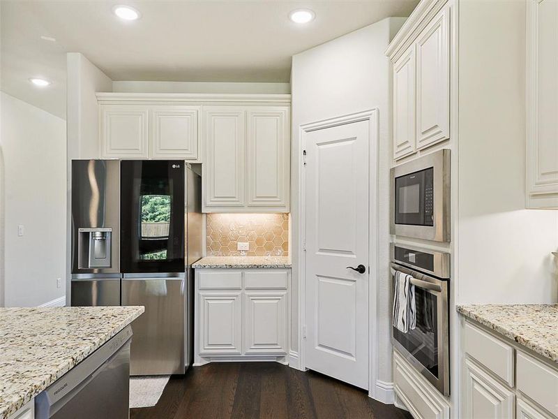 Kitchen featuring stainless steel appliances, backsplash, light stone countertops, white cabinetry, and dark hardwood / wood-style flooring