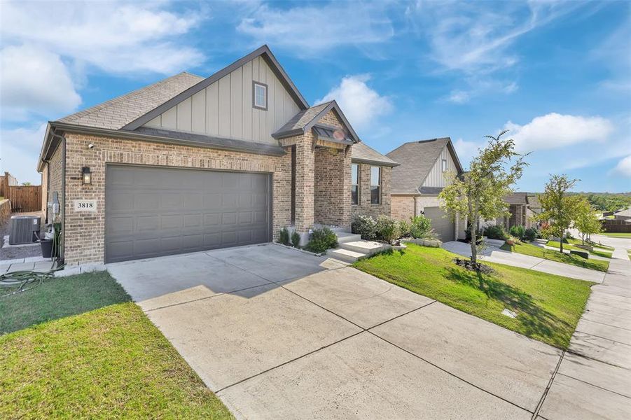 View of front of property with a front yard, central air condition unit, and a garage