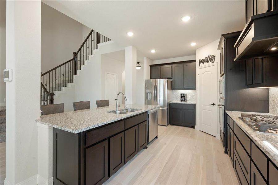 Kitchen with combination breakfast bar-island. Engineered wood flooring. White tile backsplash. Stainless steel appliances include a gas cooktop. Granite countertops.