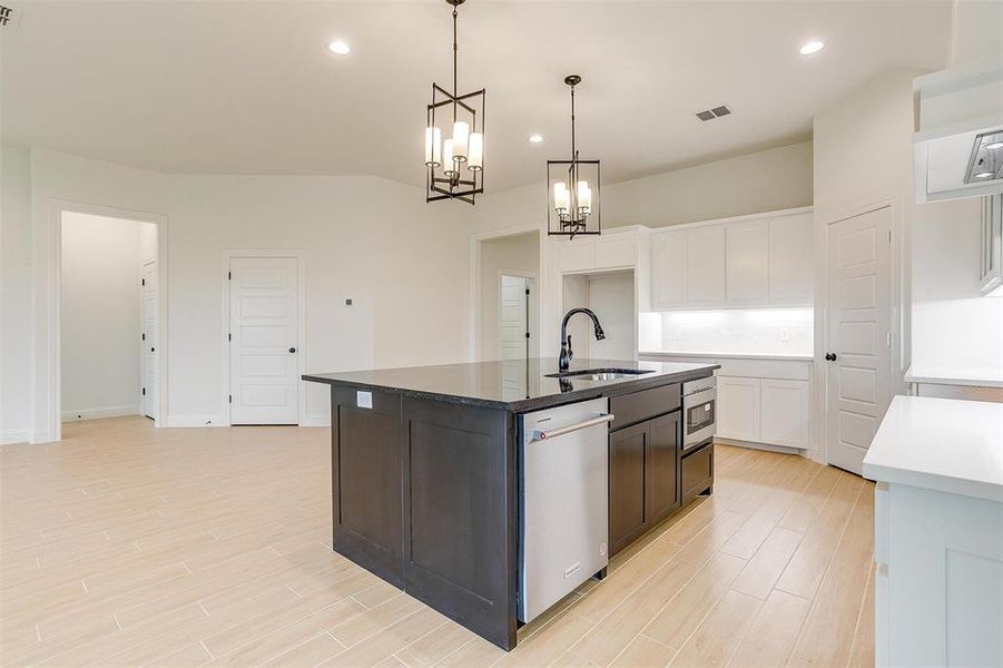 Kitchen featuring white cabinets, hanging light fixtures, sink, a kitchen island with sink, and stainless steel appliances