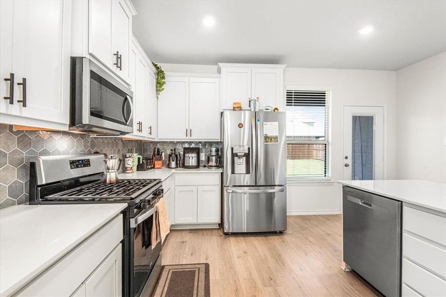 Kitchen with decorative backsplash, white cabinetry, light hardwood / wood-style flooring, and stainless steel appliances