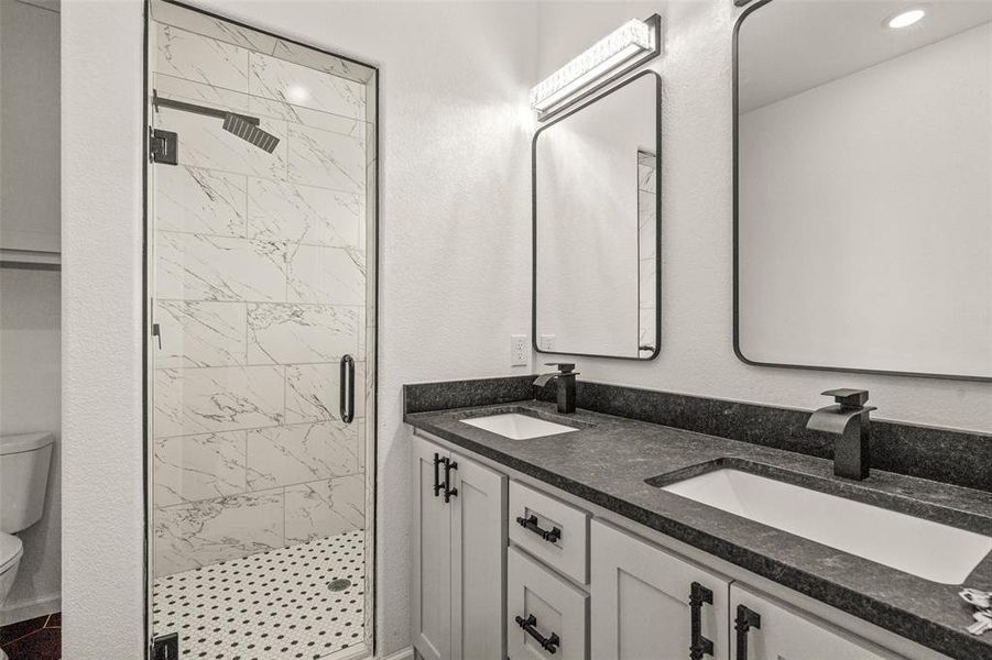 Bathroom with dual vanity, an enclosed shower, and toilet