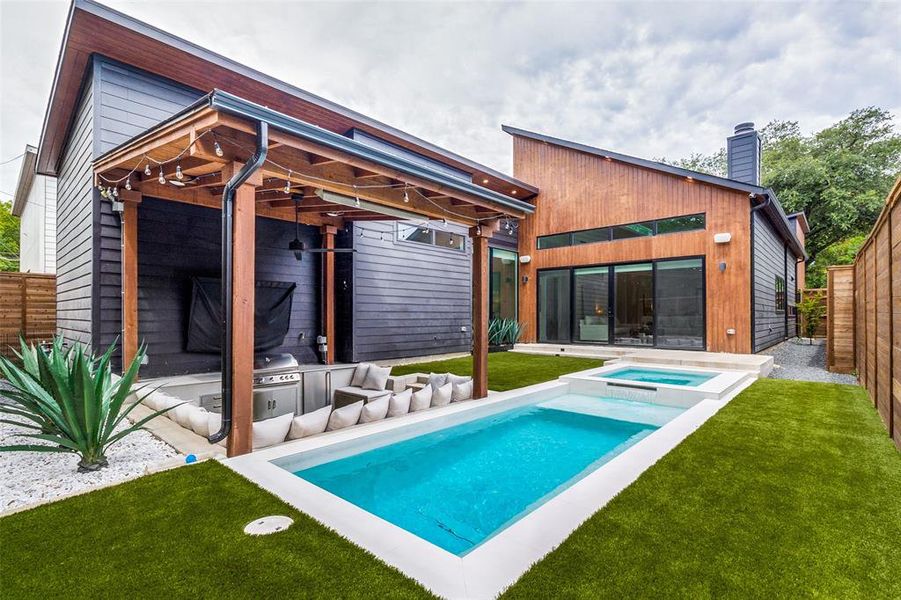 Back of property featuring a yard and a swimming pool with hot tub