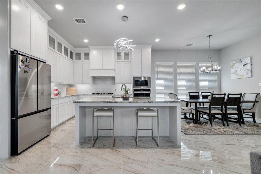 Kitchen featuring appliances with stainless steel finishes, an inviting chandelier, light stone counters, a kitchen island with sink, and a kitchen breakfast bar