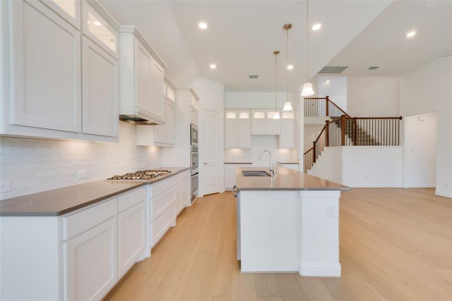 Kitchen with a center island with sink, backsplash, light hardwood / wood-style floors, and sink