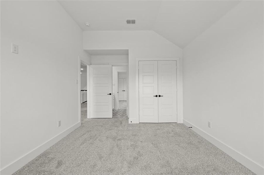 Unfurnished bedroom with a closet, light colored carpet, and vaulted ceiling