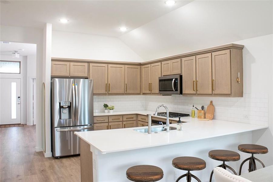 Kitchen featuring stainless steel appliances, light hardwood / wood-style floors, lofted ceiling, kitchen peninsula, and backsplash