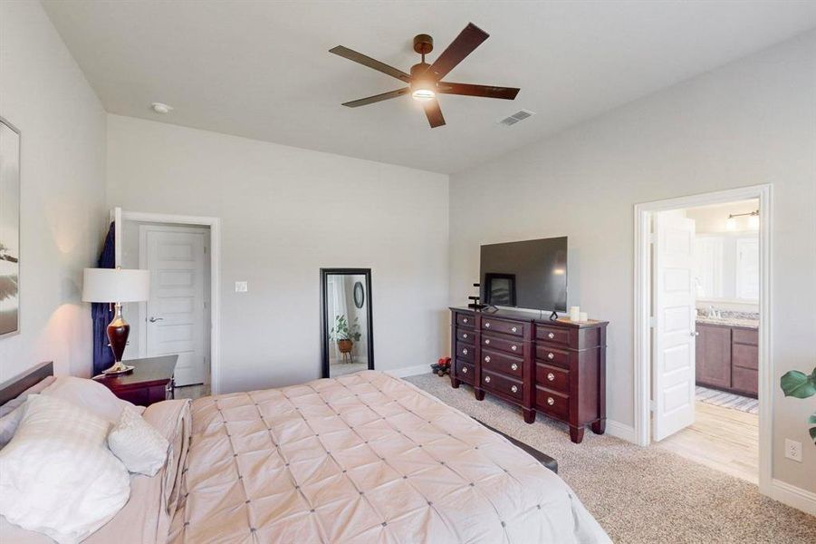 Bedroom with ensuite bath, light colored carpet, and ceiling fan