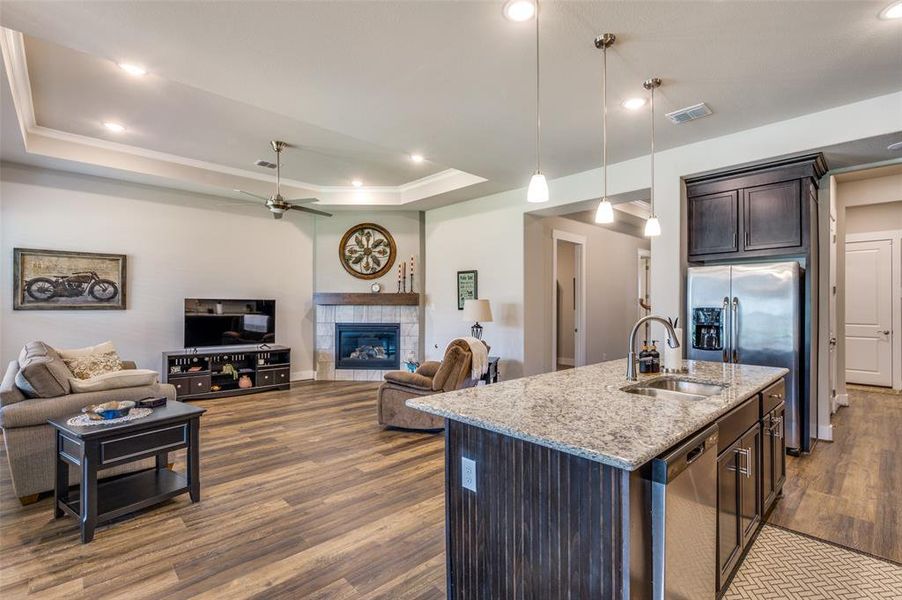 Open living area connects to kitchen and dining room for great flow.  Living room features a tray ceiling, a fireplace, wood-type flooring, sink, and a kitchen island with sink