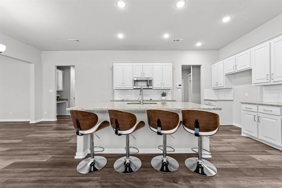 Kitchen with a center island with sink, white cabinetry, light stone counters, and dark hardwood / wood-style flooring