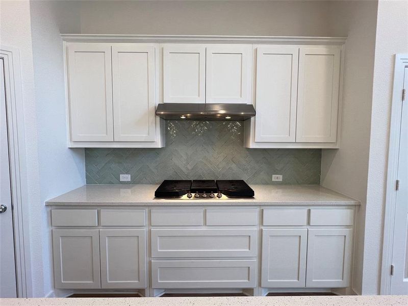 Kitchen featuring white cabinets, range hood, backsplash, and stainless steel gas cooktop