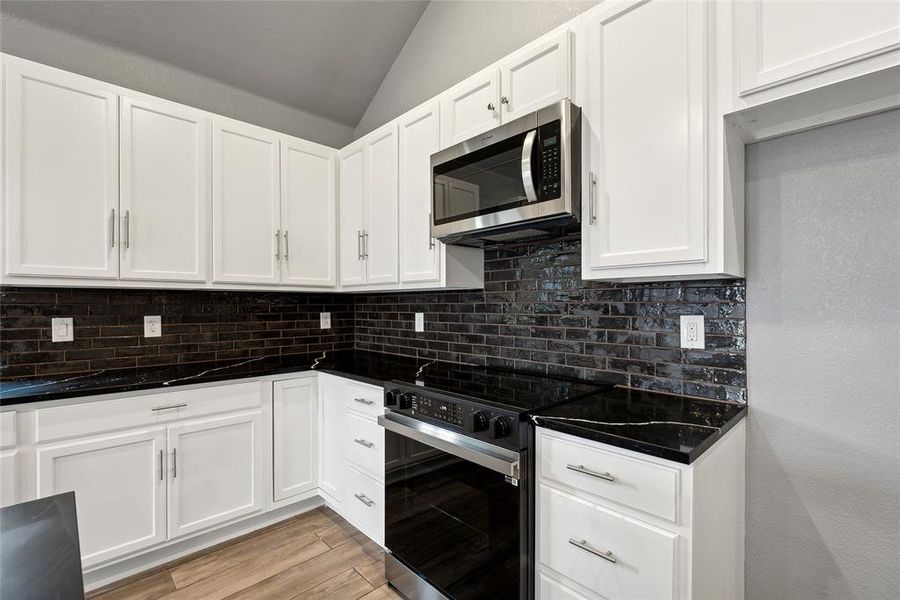 Kitchen with white cabinetry, light hardwood / wood-style flooring, stainless steel appliances, decorative backsplash, and lofted ceiling