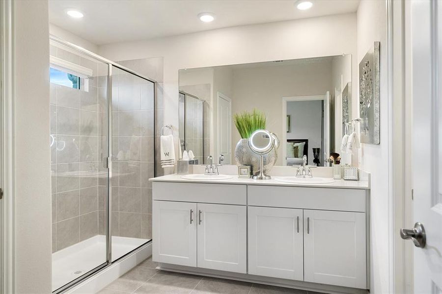 Primary bathroom featuring dual sink vanity, shower with sliding door and window offering natural light.