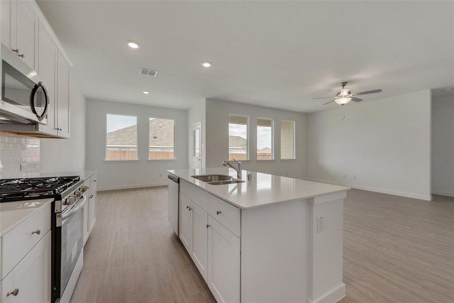 Kitchen with appliances with stainless steel finishes, white cabinetry, sink, decorative backsplash, and a kitchen island with sink