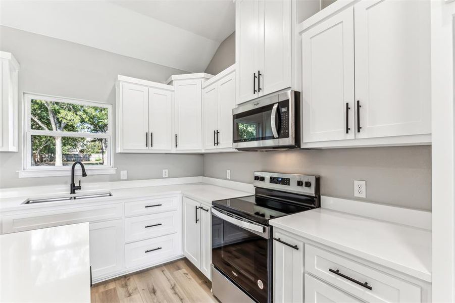 Kitchen with light hardwood / wood-style floors, stainless steel appliances, sink, white cabinetry, and lofted ceiling