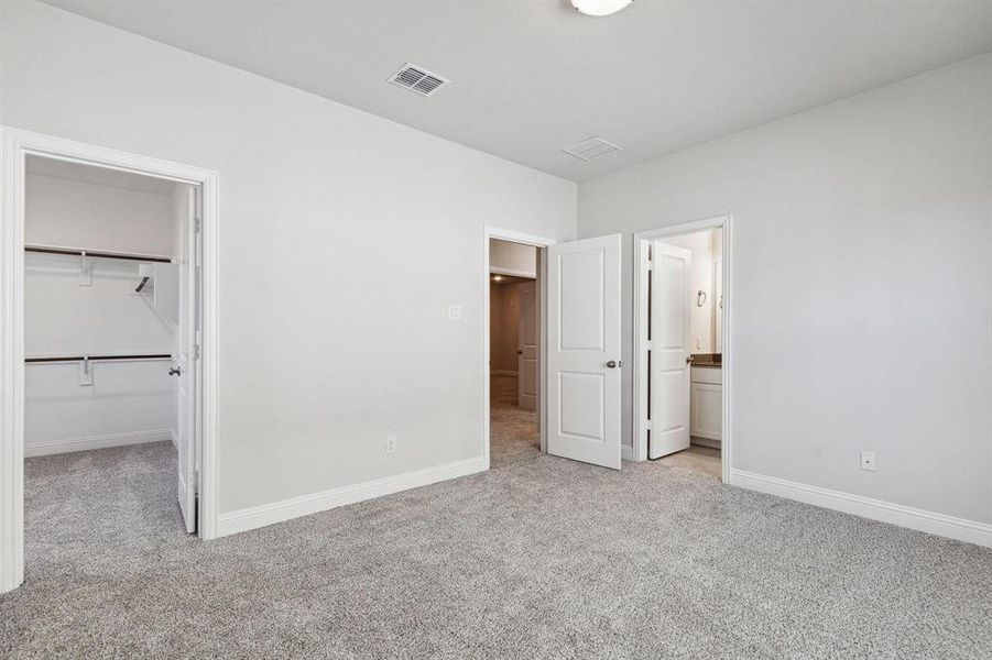 Unfurnished bedroom featuring light colored carpet, a closet, connected bathroom, and a walk in closet