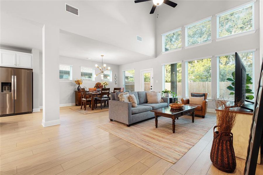 Living room featuring ceiling fan with notable chandelier, light hardwood / wood-style floors, and a towering ceiling