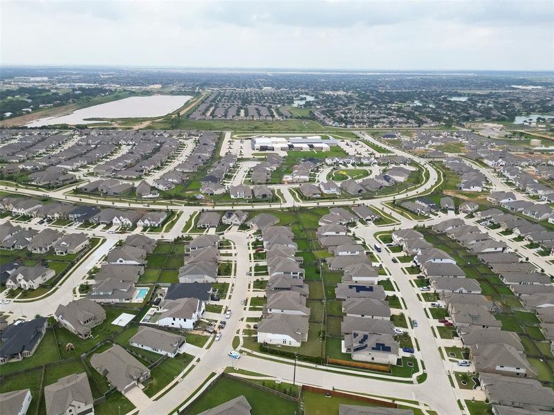 This aerial photo shows a modern, sprawling suburban neighborhood with numerous single-family homes, curving streets, and well-maintained lawns. The community is expansive, with a large pond nearby, suggesting a tranquil environment with ample space for family living.
