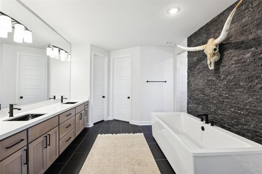 The promary bath features a double vanity with ample cabinetry, a large mirror with overhead lighting, a freestanding tub, and a separate shower area. A distinctive black textured wall adds a bold contrast, and the room is finished with a neutral color palette.