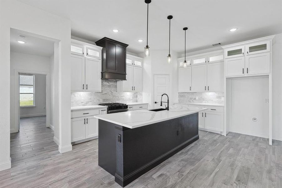 Kitchen featuring a kitchen island with sink, stainless steel gas stove, and white cabinets