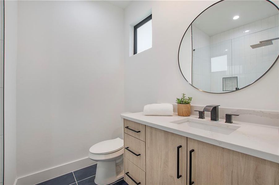 Bathroom featuring tile patterned flooring, vanity, toilet, and a shower