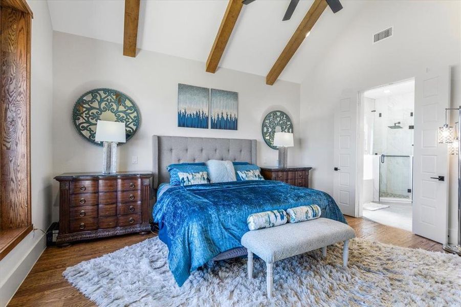 Bedroom featuring beamed ceiling, dark wood-type flooring, high vaulted ceiling, ensuite bathroom, and ceiling fan