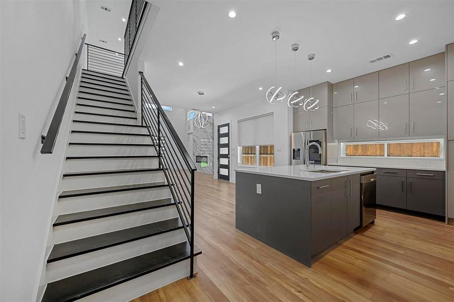 Kitchen with an island with sink, gray cabinetry, decorative light fixtures, and light hardwood / wood-style floors