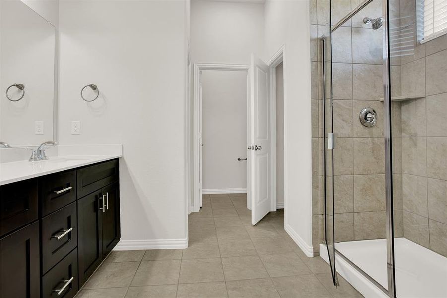 Bathroom with tile floors, a shower with shower door, and vanity