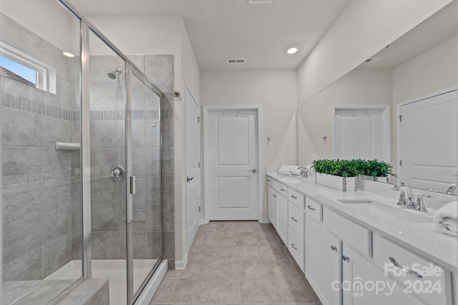 Primary bathroom view from Primary bedroom to closet door. Beautiful neutral colors, upgraded countertops and tile shower.