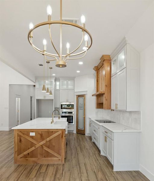 Kitchen featuring light wood-type flooring, an island with sink, pendant lighting, white cabinets, and decorative backsplash