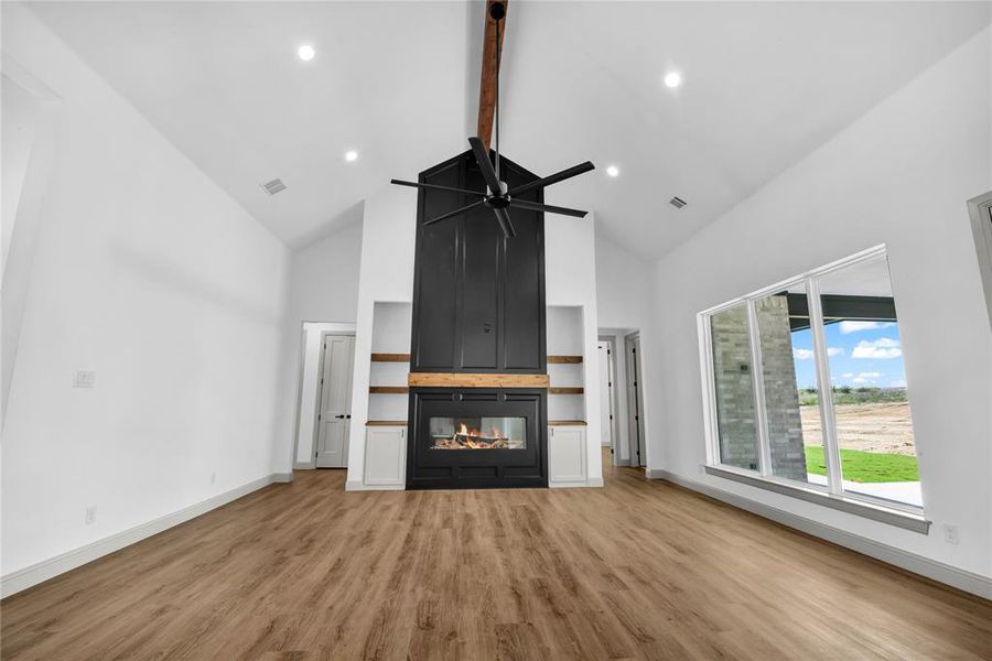 Unfurnished living room featuring ceiling fan, beamed ceiling, a multi sided fireplace, high vaulted ceiling, and light hardwood / wood-style floors