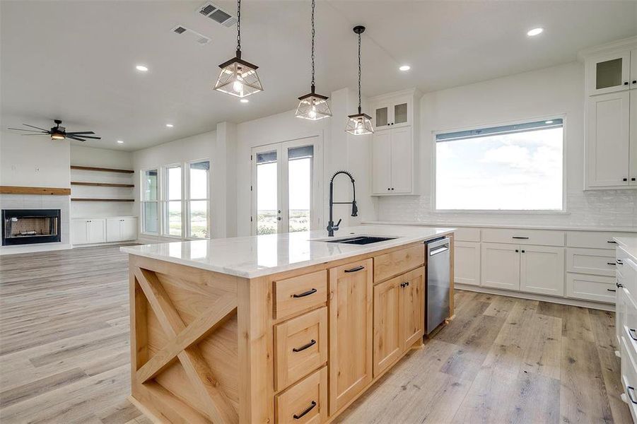 Kitchen with a tiled fireplace, white cabinetry, sink, ceiling fan, and a center island with sink