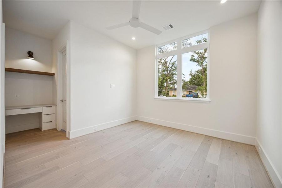 The first floor ensuite guest room has a large walk-in closet with a window that keeps it well-illuminated. A built-in desk with floating shelf and attractive lighting add form and function.