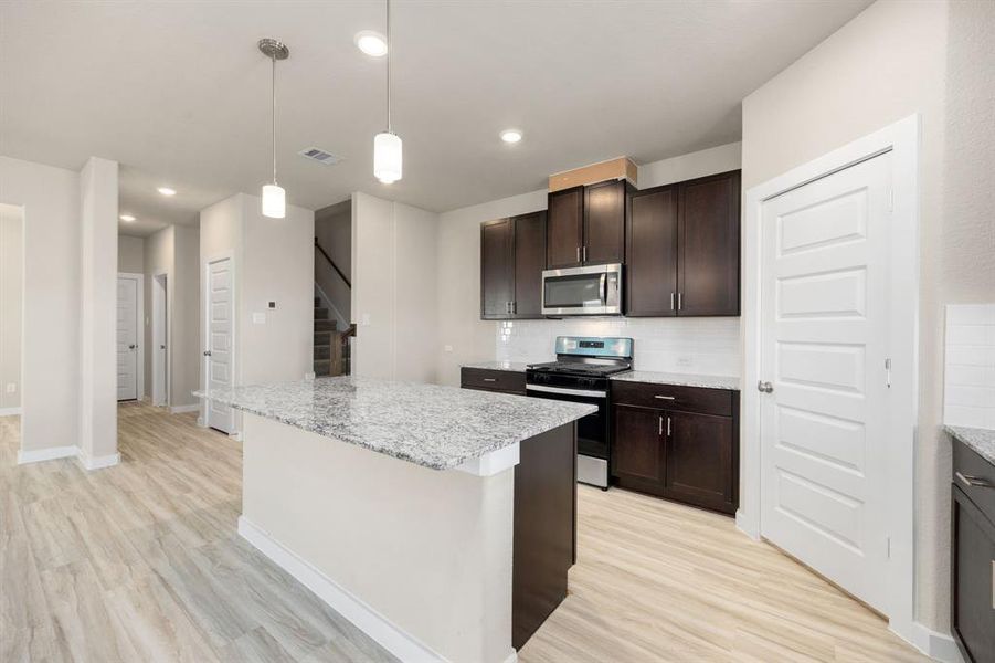 This stunning kitchen displays such a beautiful ambience with the dark cabinets, neutral paint, Granite countertops, light modern backsplash, and SS appliances, oversized kitchen island with extra storage, breakfast bar, recessed lighting, high ceilings and pantry.