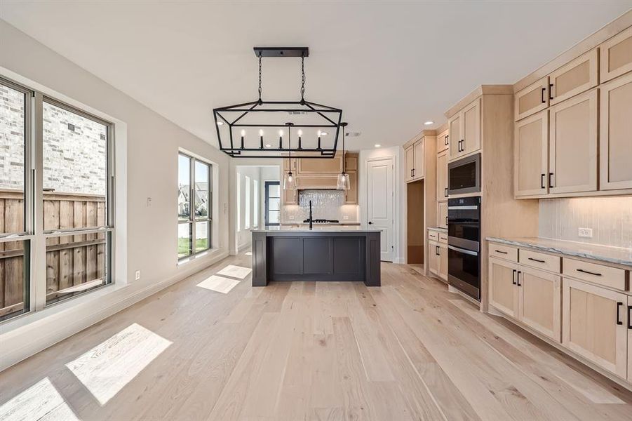 Kitchen with pendant lighting, tasteful backsplash, a chandelier, appliances with stainless steel finishes, and light wood-type flooring