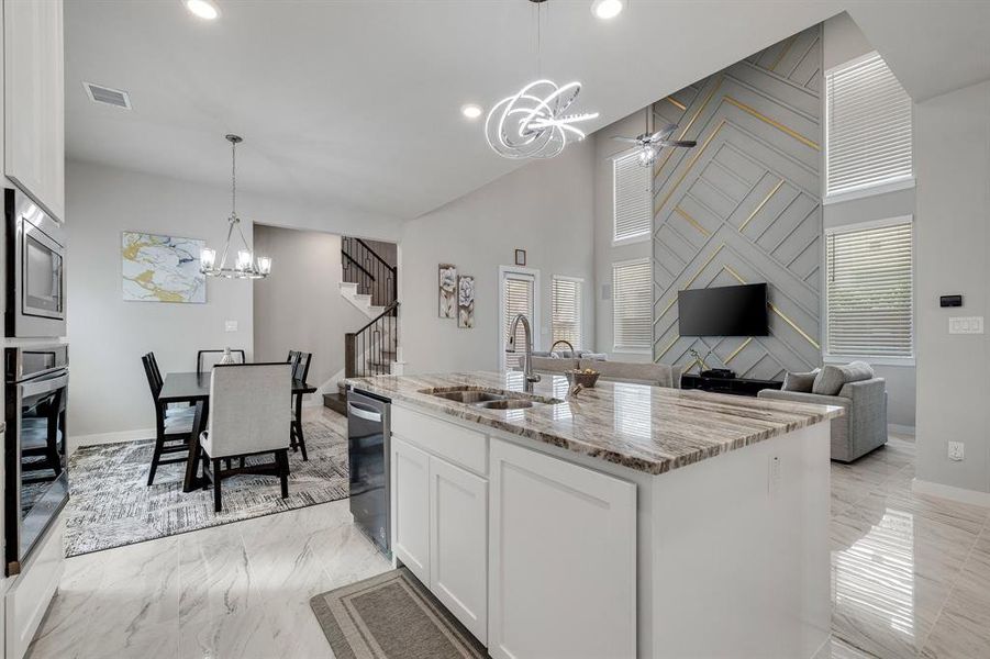 Kitchen with stainless steel appliances, white cabinets, sink, light stone counters, and ceiling fan with notable chandelier