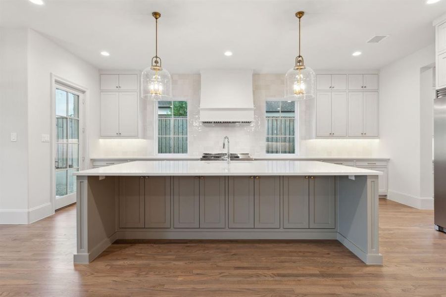 Kitchen featuring white cabinetry, custom range hood, hardwood / wood-style floors, and a large island with sink