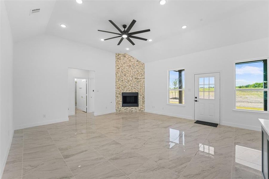 Unfurnished living room featuring high vaulted ceiling, ceiling fan, a fireplace, and light tile flooring