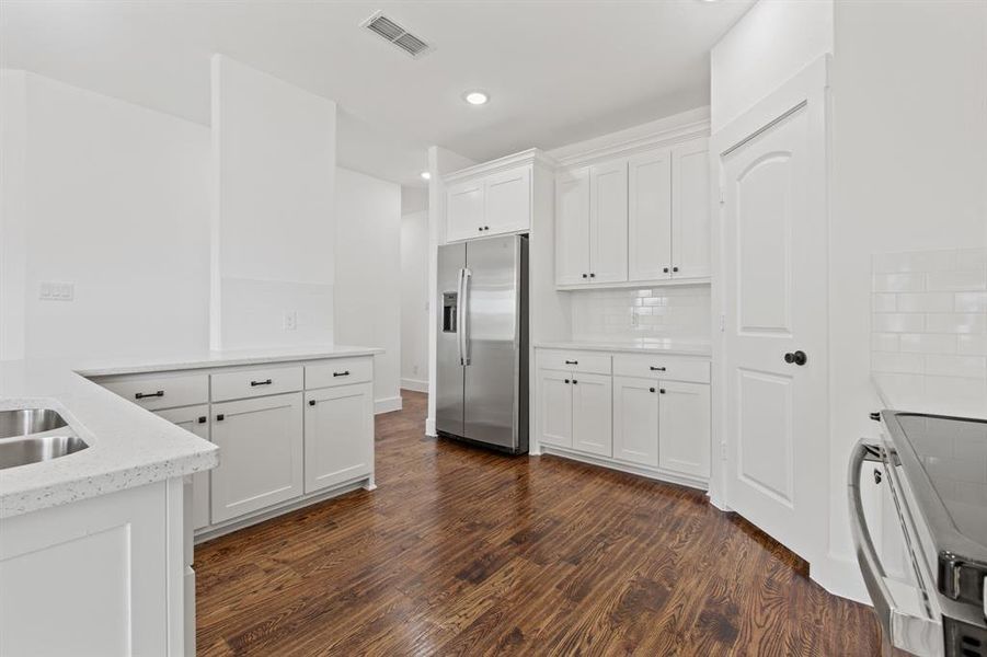 Kitchen with stainless steel fridge, white cabinetry, stove, dark hardwood / wood-style flooring, and light stone countertops