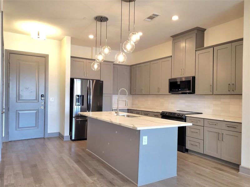 Kitchen with tasteful backsplash, stainless steel appliances, light wood-type flooring, hanging light fixtures, and sink