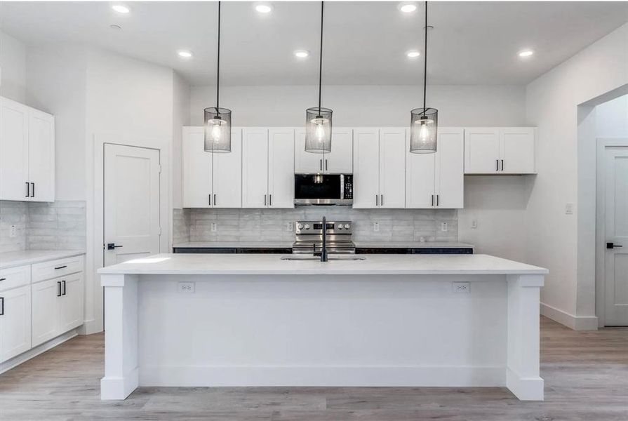 Kitchen featuring appliances with stainless steel finishes, decorative light fixtures, and an island with sink