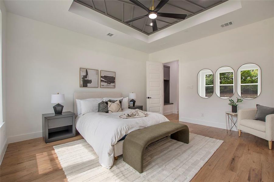 Bedroom with light hardwood / wood-style floors, a raised ceiling, a high ceiling, and ceiling fan