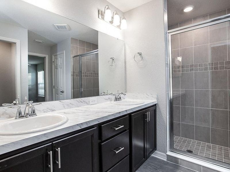 Dual vanity en-suite bath with a decorative tiled shower with glass enclosure - Photo showcases a home with similar finishes. Colors and design options in actual home for sale may differ.